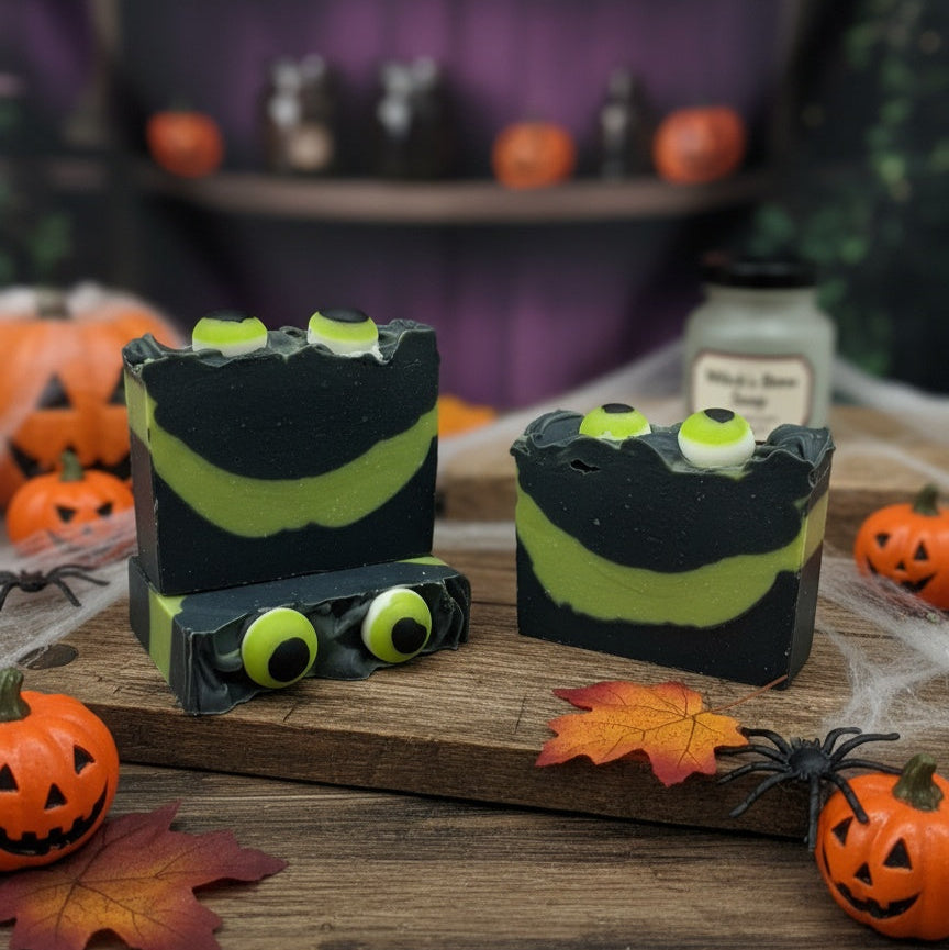 Halloween-themed soap bars with candy eyes on a wooden board, surrounded by pumpkins and leaves.